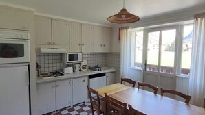 Una cocina compacta con armarios blancos, una mesa de comedor de madera y una ventana con cortinas.