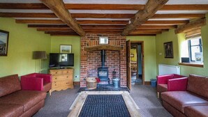 Ein gemütliches Zimmer mit Kamin, Holzbalken, grünen Wänden und Ledersofas.