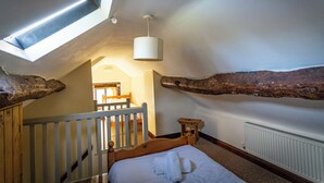 Ein Schlafzimmer mit schrägem Dach, einem Oberlicht, einem hölzernen Bett, einer weißen Heizung und einer Holzbank.