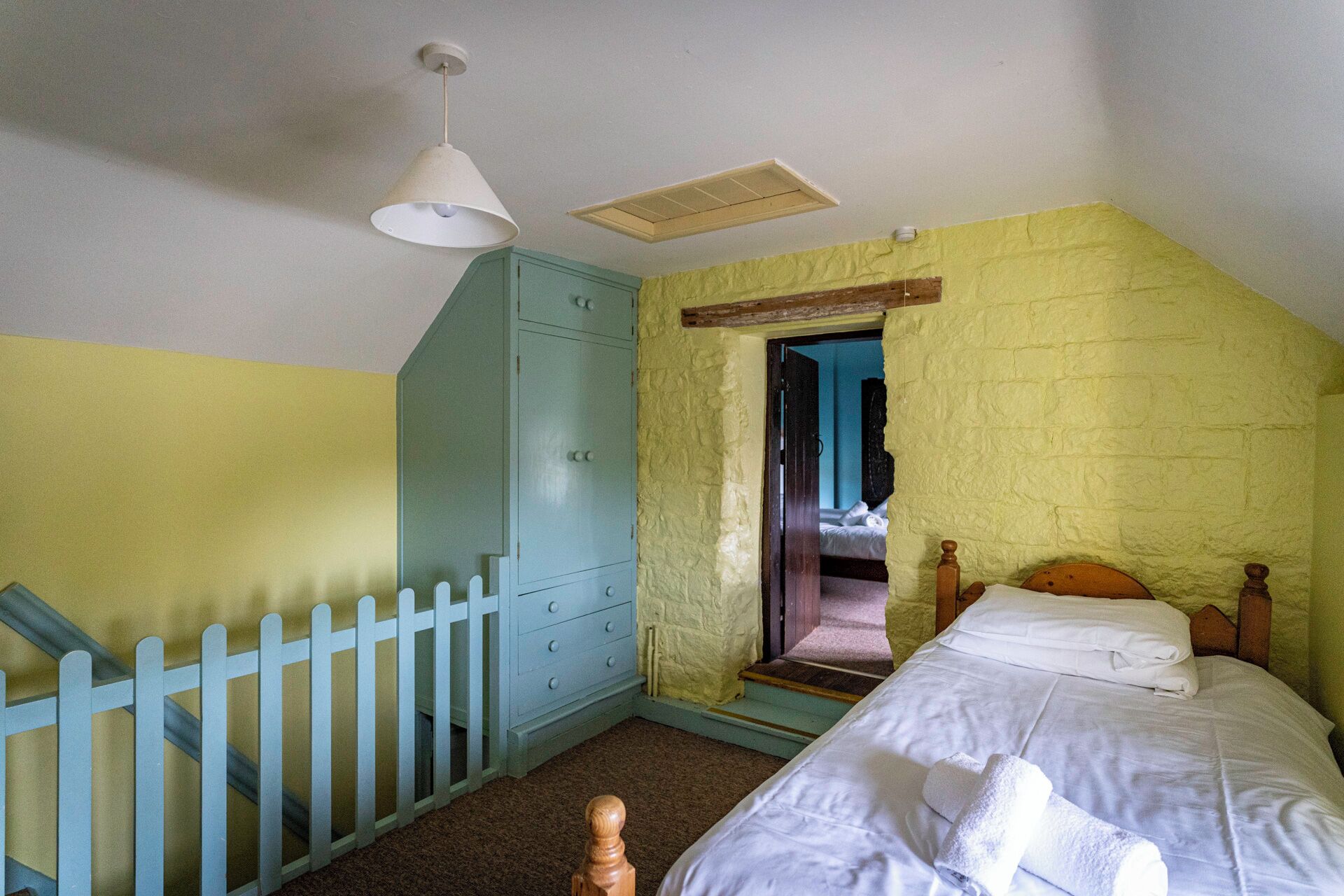 A bedroom with a bed, a wooden wardrobe, a white ceiling fan, and a white door leading to another room.