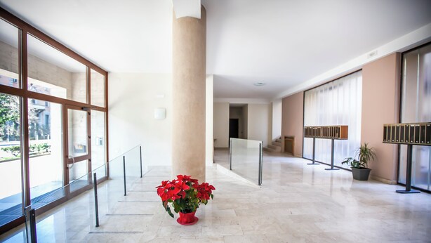 Un'ampia hall con pavimento in marmo, grandi finestre e una colonna centrale.