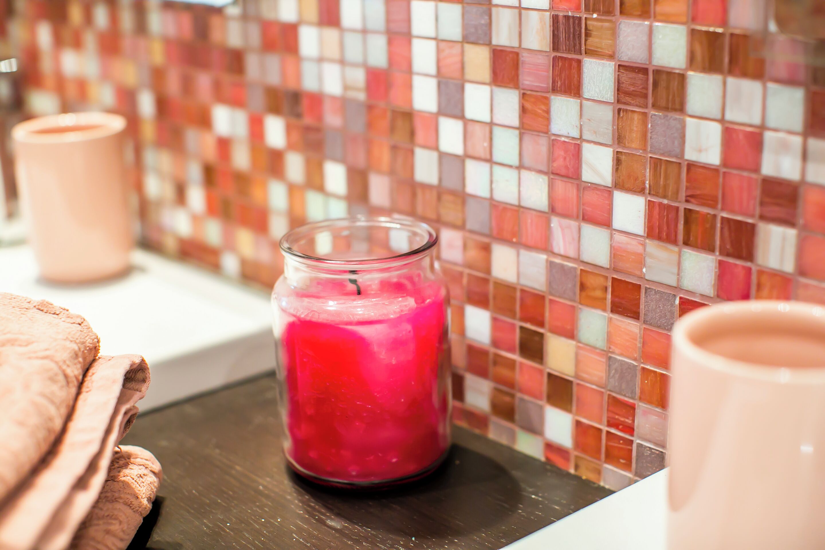 A bathroom with a mosaic tile wall, a glass jar with a pink liquid, and a towel.