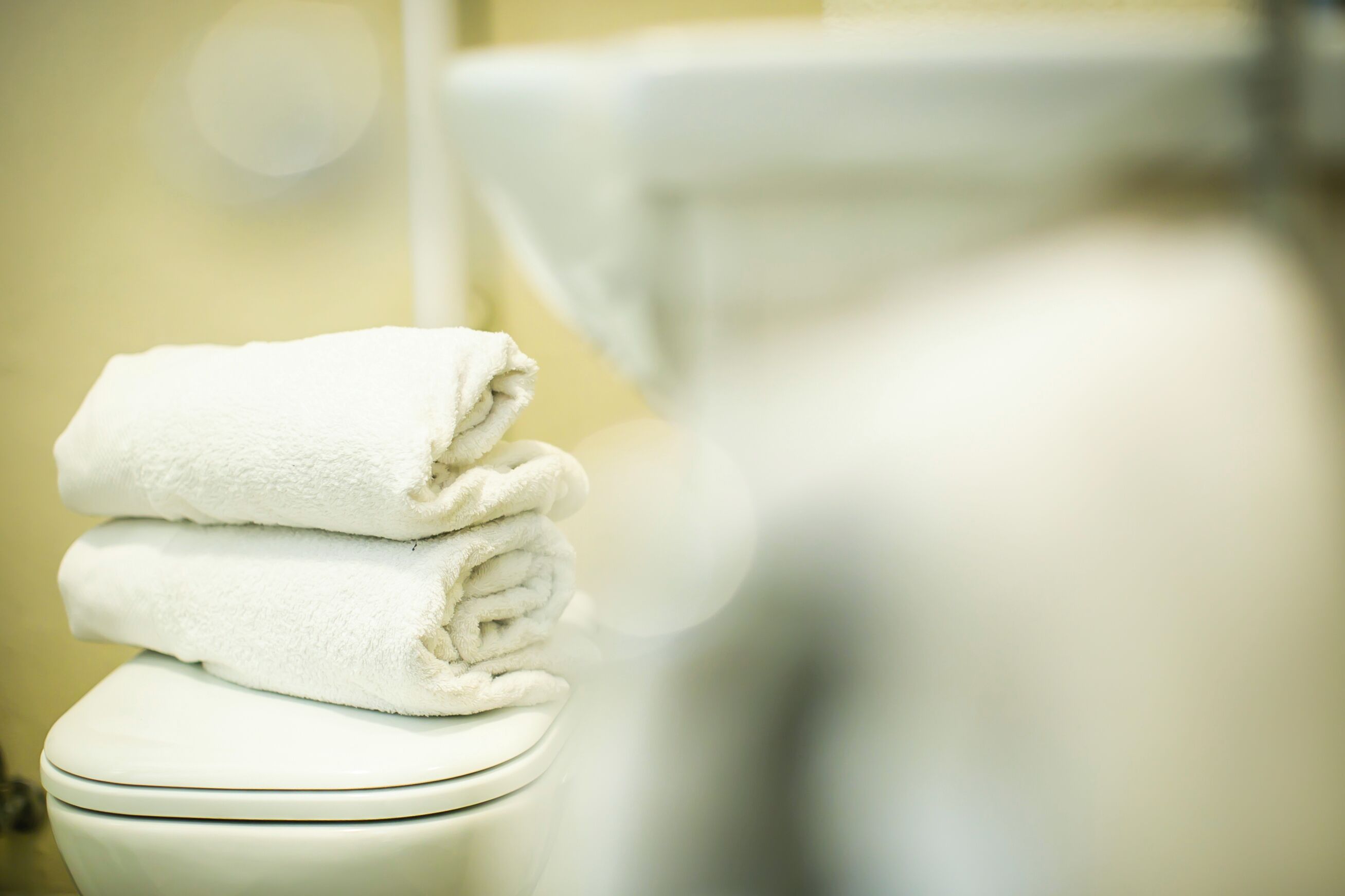A stack of white towels on a toilet seat in a bathroom.