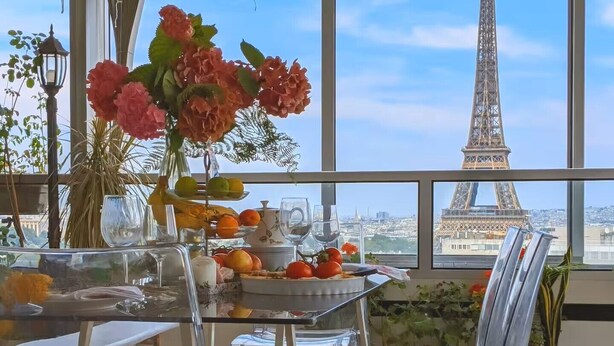 A dining area with a table set for two, a vase of flowers, and a view of the Eiffel Tower.