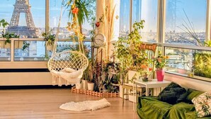 A room with a view of the Eiffel Tower, a hanging chair, a green sofa, and various potted plants.