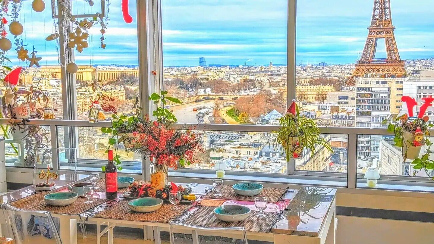 A dining area with a view of the Eiffel Tower, a table set with plates and glasses, and potted plants.