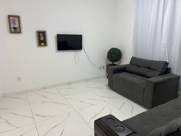 Un salón con un sofá gris, un televisor de pantalla plana en la pared y una pequeña planta en maceta.
