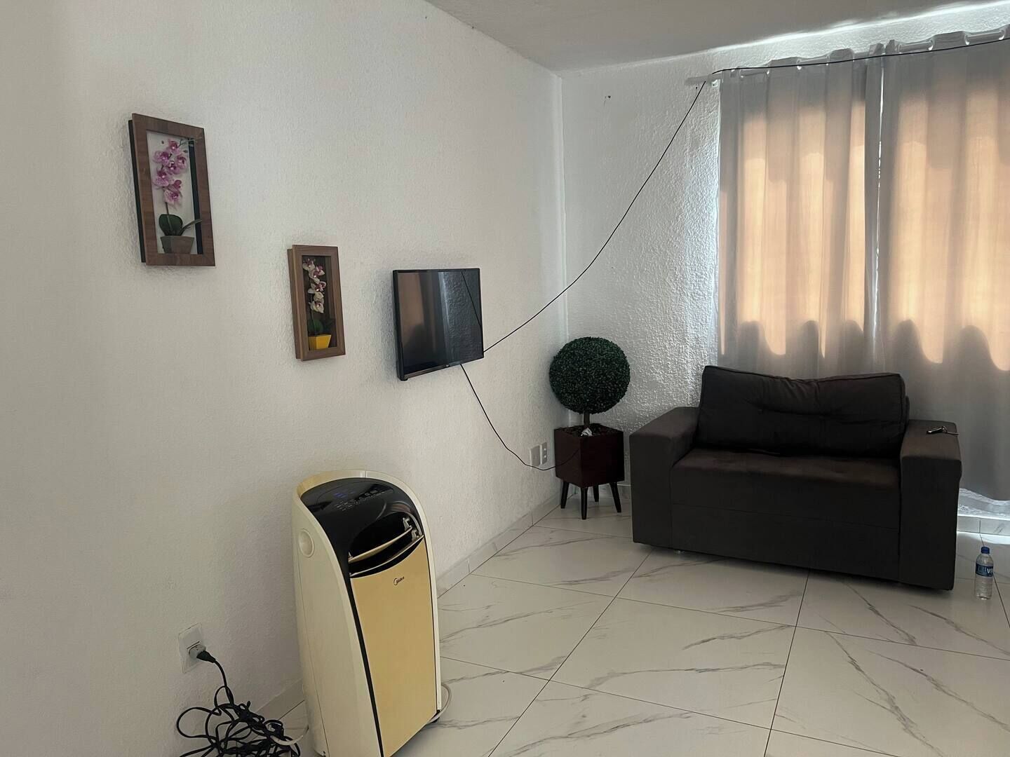 A living room with a sofa, a small table with a potted plant, a television mounted on the wall, and a speaker.