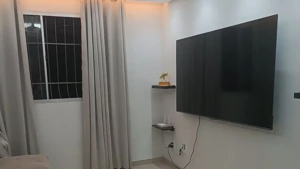 A modern living room with a flat-screen TV mounted on the wall, a ceiling fan, and a window with curtains. - 1 Near Confins Airport, Cid Galo, 15 min BH, Cid Adm.  (Centro Vespasiano)