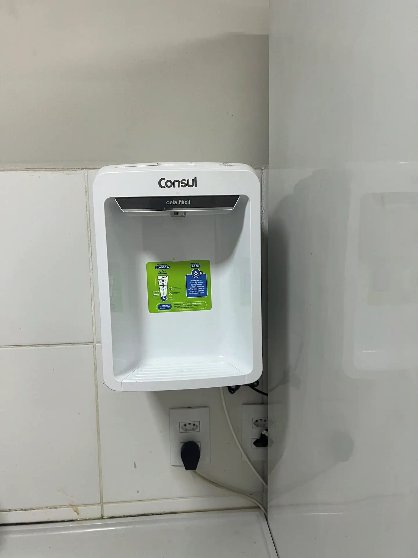 A white wall-mounted dispenser with a green label, a power outlet, and a switch below it.