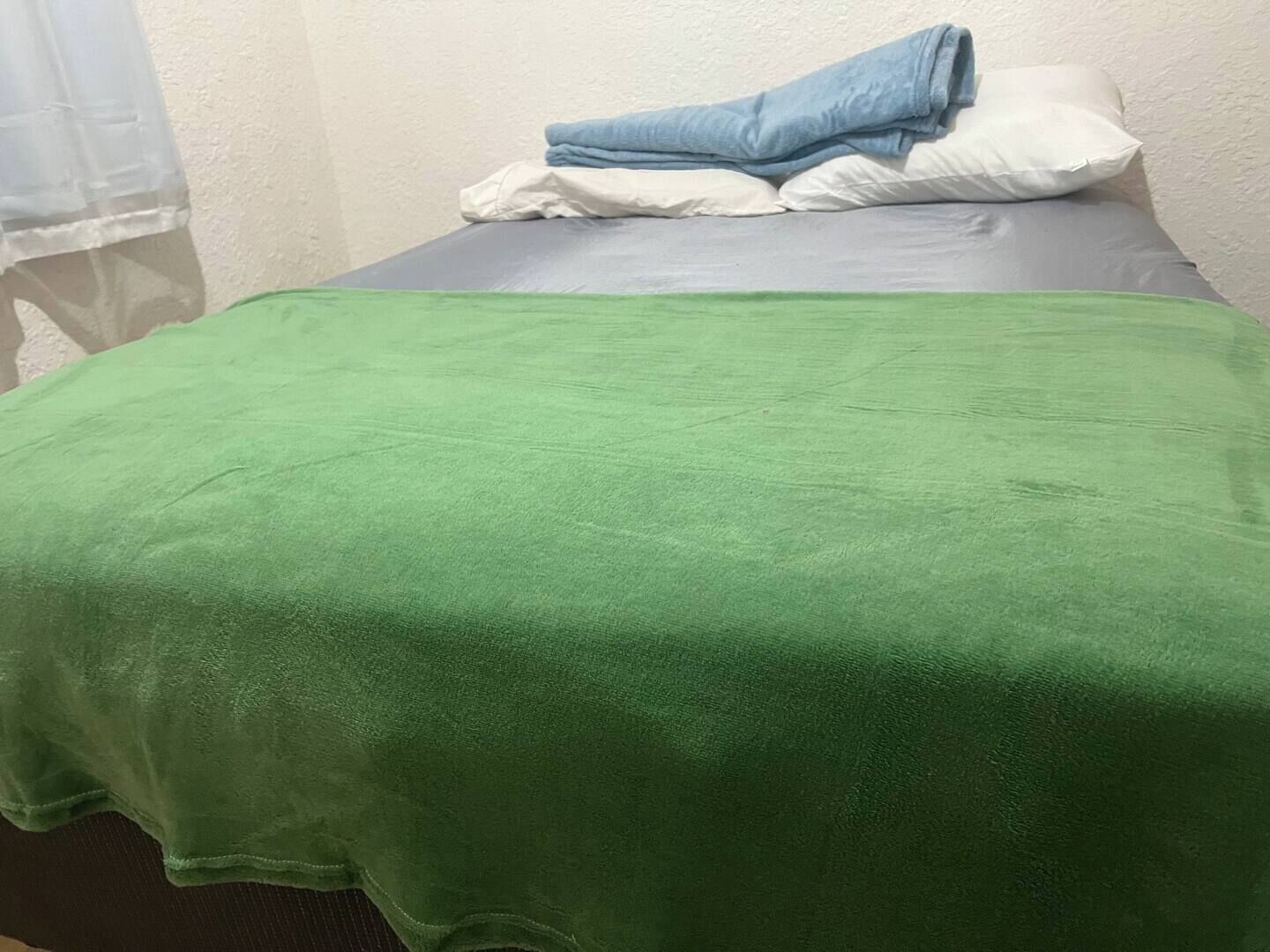 Una cama individual con una manta verde, almohadas blancas y una toalla azul.