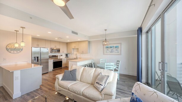 A modern kitchen with stainless steel appliances, a dining area with a white table and chairs, and a living room with a beige sofa and a glass coffee table. - NEW! Waterfront Luxury in Sarasota – Near Downtown & Beaches! (Sarasota)