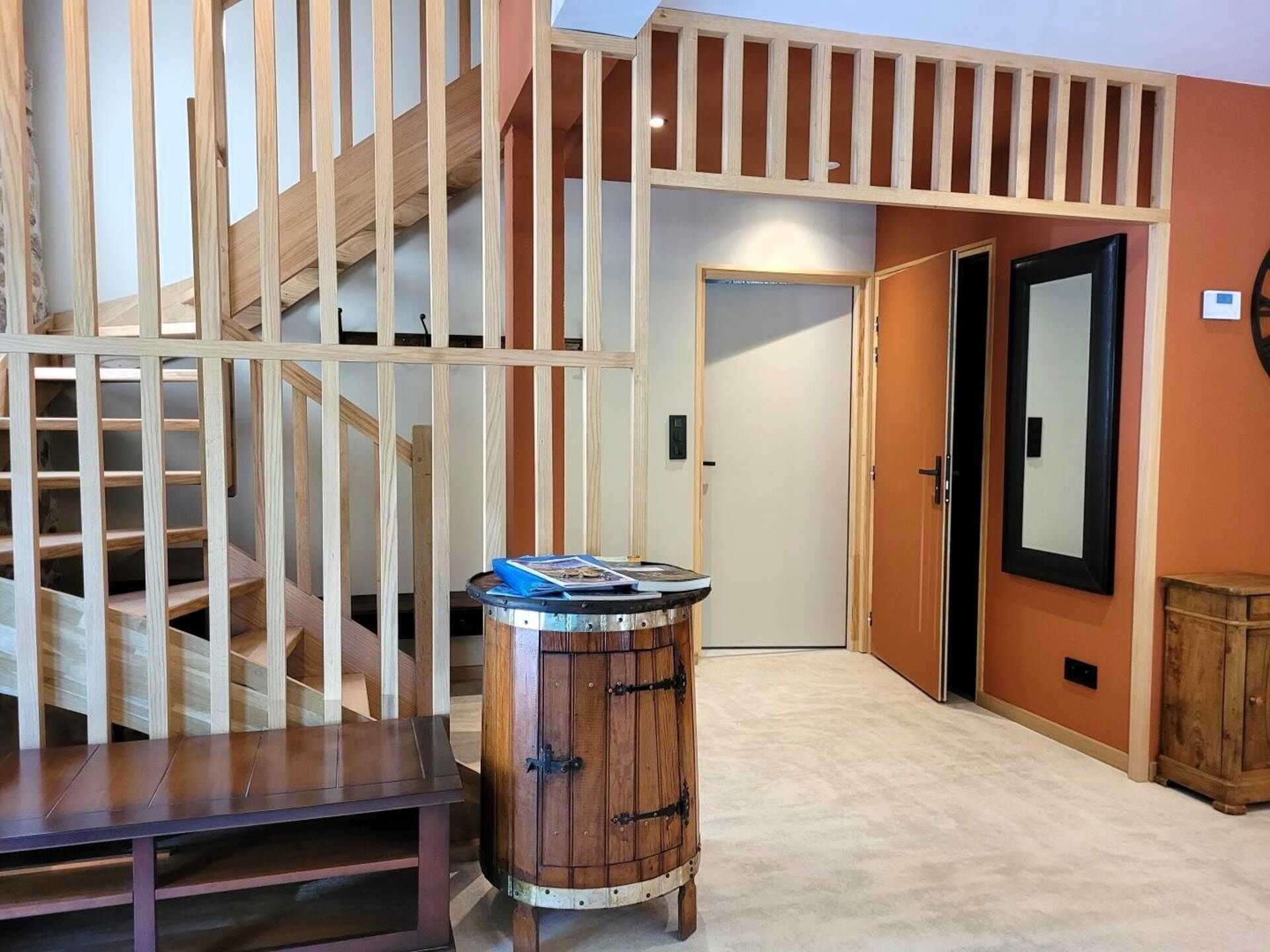 A staircase with wooden railings, a round wooden barrel with a blue object on top, and a door with a black frame.
