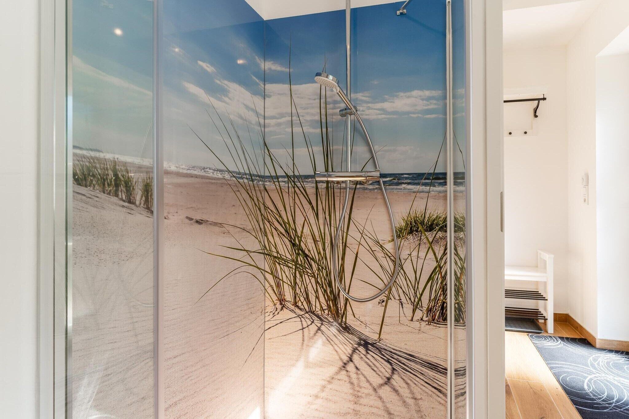 A modern bathroom with a glass shower enclosure, a view of the beach, and a minimalist design.