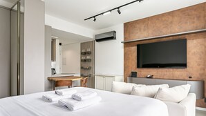 A modern hotel room with a large bed, a flat-screen TV mounted on the wall, a wooden desk, and a seating area with a chair. - WI-FI 500mb | 65" Smart TV | Pool #CAMP10 (Florianópolis)