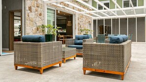 A spacious outdoor seating area with wicker furniture and a stone wall backdrop. - WI-FI 500mb | 65" Smart TV | Pool #CAMP10 (Florianópolis)