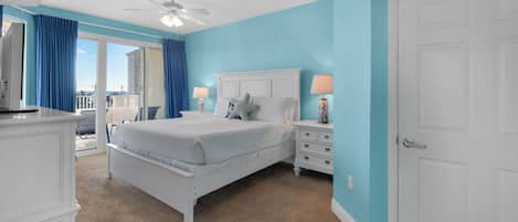 Une chambre à coucher comprenant un lit, des tables de chevet, une commode, un ventilateur de plafond et une vue sur l’extérieur.