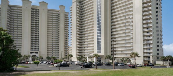 A multi-story hotel with a central entrance, surrounded by parking and palm trees. - Prime Gulf View Condo Near top Attractions, Dining, & Beach Fun! (Miramar Beach)
