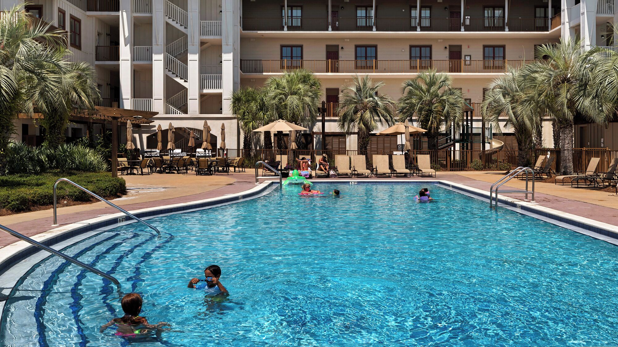 A swimming pool with multiple levels of balconies, palm trees, and lounge chairs.