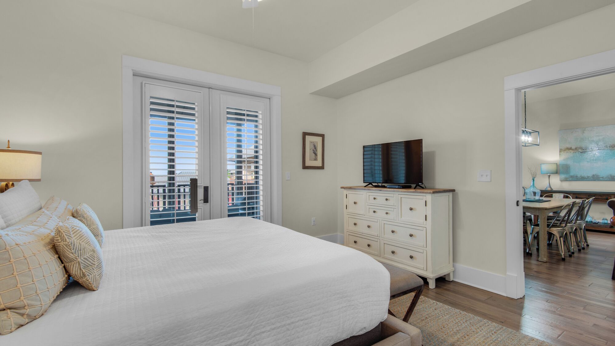 A bedroom with a large bed, a dresser, a television, and a dining area with chairs and a table.