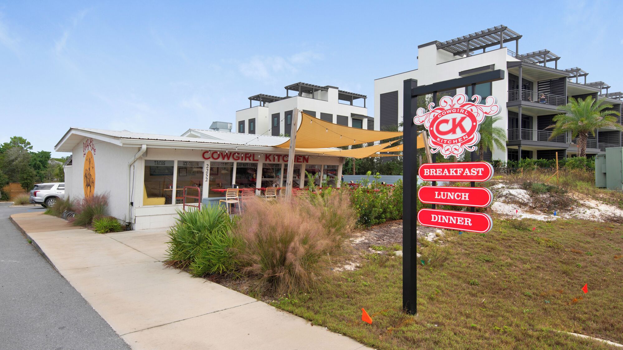 A restaurant named 'Cowgirl Kitchen' with outdoor seating and a sign indicating breakfast, lunch, and dinner services.
