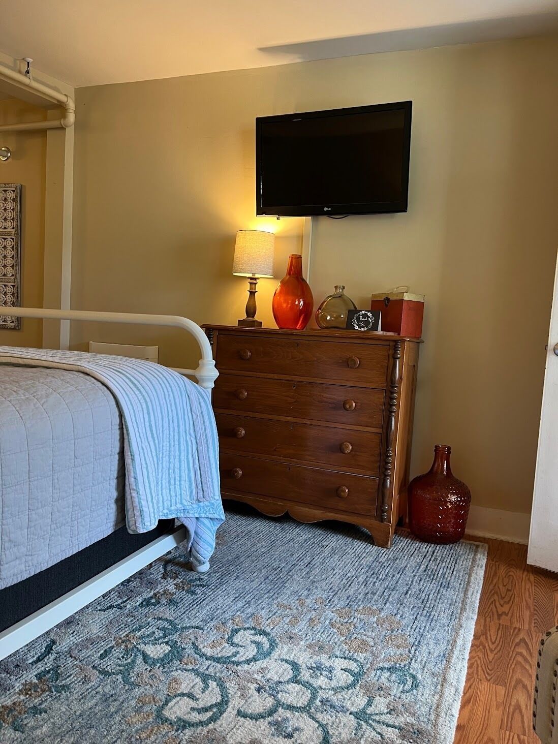 A bedroom with a bed, a dresser, a television mounted on the wall, and a patterned rug.