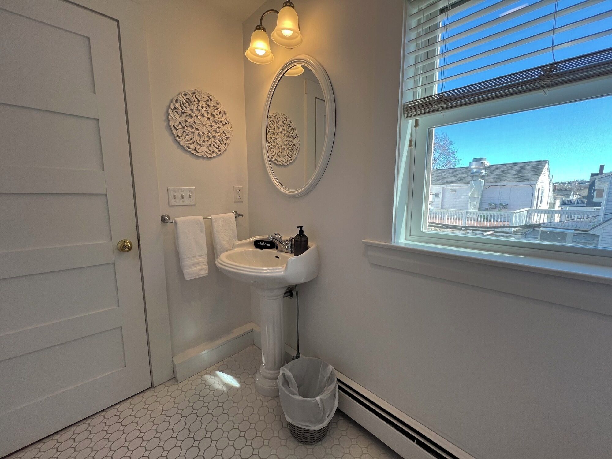 Un baño con lavamanos blanco, espejo y ventana con vistas a edificios.