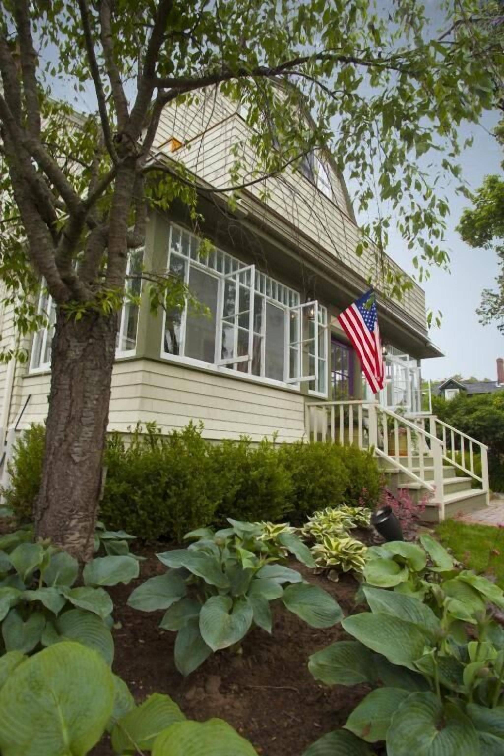 A house with a porch, an American flag, and a garden with various plants.