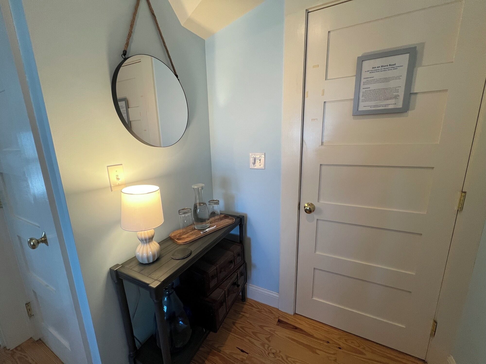 A bathroom with a wooden vanity, a mirror, a wall-mounted light, and a door with a sign.