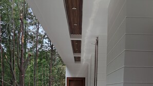 A corridor with a wooden ceiling, white walls, and a metal railing overlooking a forested area. - JAMUNAS B&B (Shimla)