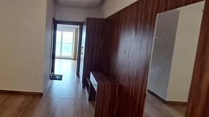 A hallway with wooden flooring, a door on the right, and a view into a room with a large window. - JAMUNAS B&B (Shimla)