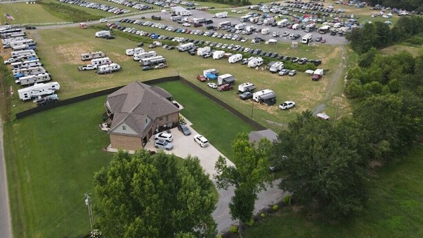 An aerial view of a large RV park with multiple rows of RVs and trailers, a central building, and surrounding greenery. - Walk to ROCK THE SOUTH RV Camping with Generator 4 Night Package Cullman Alabama (Cullman)