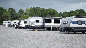 A row of RVs parked on a gravel surface with trees in the background. - Walk to ROCK THE SOUTH RV Camping with Generator 4 Night Package Cullman Alabama (Cullman)