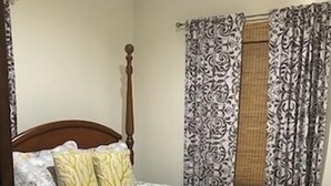 Un dormitorio con estructura de cama de madera, colcha estampada y cortinas con diseño.
