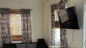 Una sala de estar con un sofá oscuro, una mesa de centro de madera y cortinas estampadas.