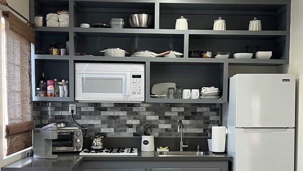 Una cocina compacta con gabinetes grises, un microondas blanco, un horno integrado y un refrigerador blanco.