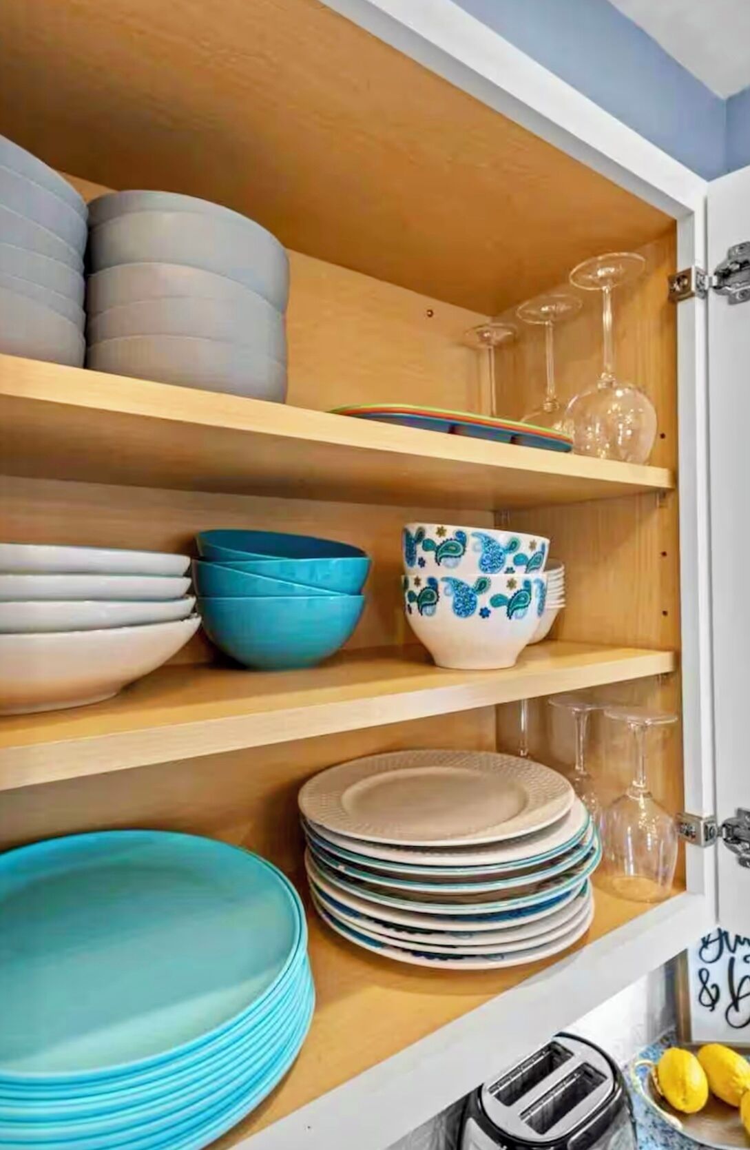 A kitchen cabinet with multiple shelves holding plates, bowls, and glasses.