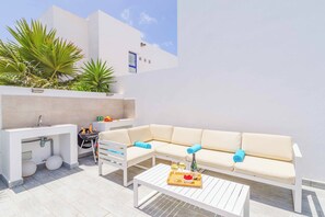 A modern outdoor living area with a white sofa, a dining table, and a grill. - Villa Elizabeth Rubicon (Yaiza)