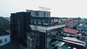 A hotel with a prominent sign reading "Grand Pallado Hotel & Suites." It features a modern architectural design with a flat roof and a glass facade. - Grand Pallazo Hotel and Suites (Lagos)