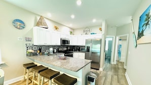 A modern kitchen with white cabinets, a granite countertop, and a stainless steel refrigerator.