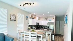A modern kitchen with white cabinets, a stainless steel refrigerator, and a dining area with a wooden table and white chairs.