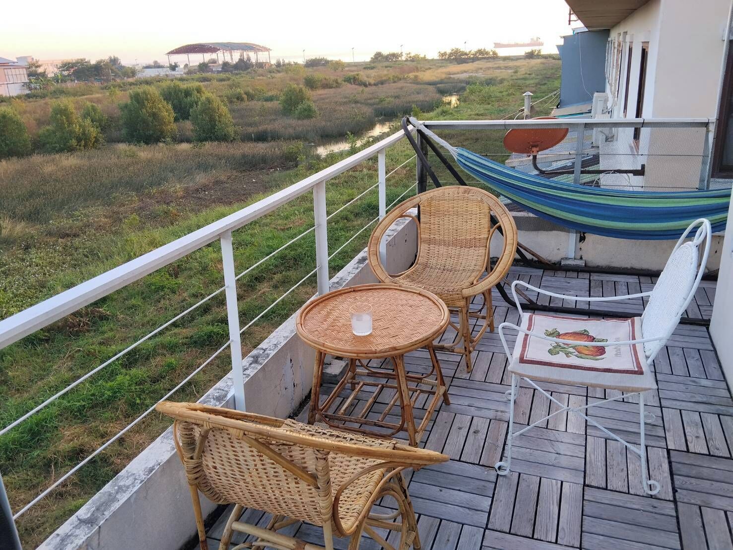 Un balcon agrémenté de meubles en osier, d’un hamac et offrant une vue sur un paysage naturel.