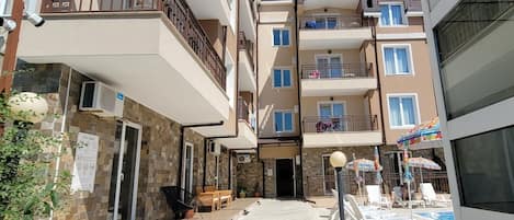 Un edificio residencial de varios pisos con balcones, un área de piscina con sillones de descanso y fachada de piedra.