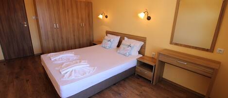 A bedroom with a bed, wooden wardrobe, bedside table, and a mirror.