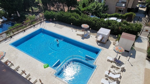 Piscina en la azotea con trampolín, rodeada de sillas y sombrillas de descanso.