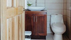 A bathroom with a wooden cabinet, a white sink, and a toilet. - Cabinas El Quetzal (Copey)