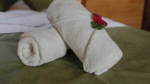 A neatly made bed with a green blanket and two rolled white towels, one with a red flower decoration. - Cabinas El Quetzal (Copey)