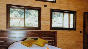 A wooden-paneled bedroom with a bed, two windows, and a door. - Cabinas El Quetzal (Copey)
