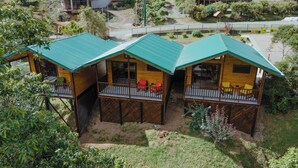 Three wooden cabins with green roofs, each featuring a balcony with red chairs. - Cabinas El Quetzal (Copey)