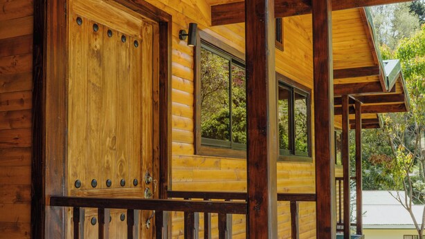 A wooden log cabin with a porch, a large wooden door, and a window. - Cabinas El Quetzal (Copey)